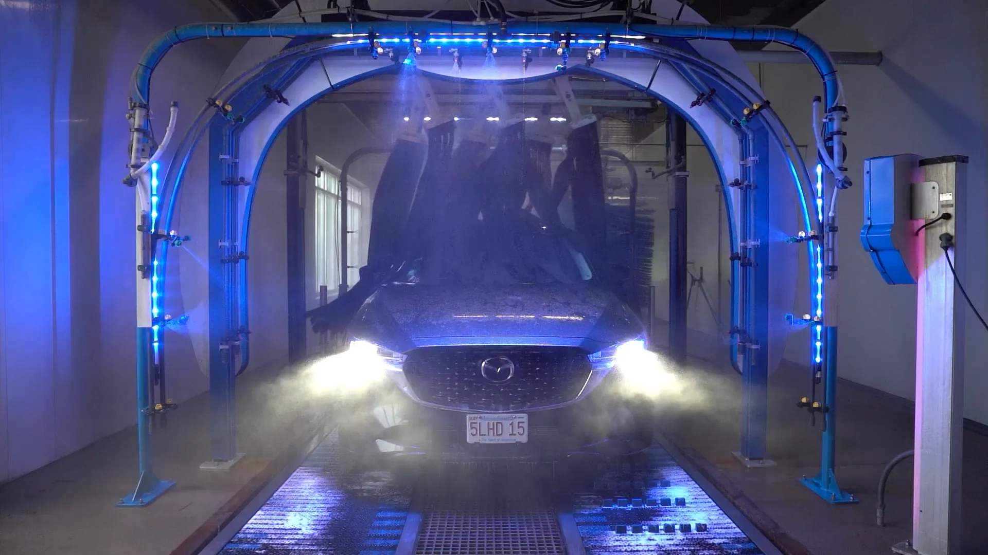A car being cleaned under blue lights inside a Jilly's Car Wash